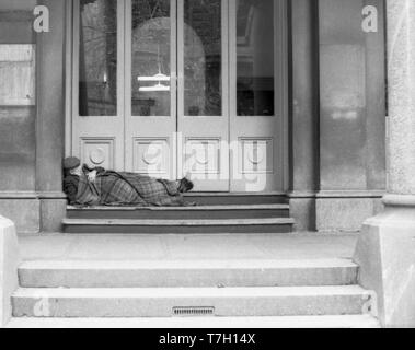 1977 Martin Place, Sydney Australia: An older male person, possibly a vagrant or homeless person sleeps in one of the timber doorways of Sydney's GPO (General Post Office). Around this time it was common for homeless people to sleep in similar places away from rain and wind. Stock Photo