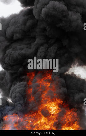 Huge flames of red-orange fire, motion clouds of dark smoke covered sky. Selective focus, motion blur, haze from strong fire and high temperature from Stock Photo