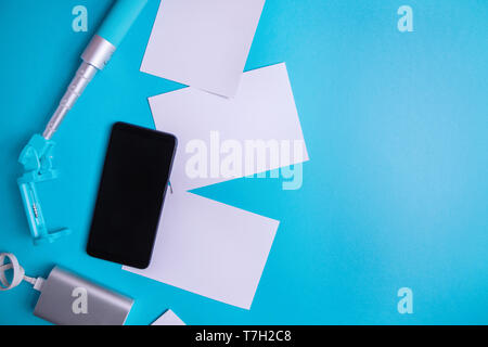 Smartphone with blank screen and flyers and photos on a blue background. Mock up, flat lay Stock Photo