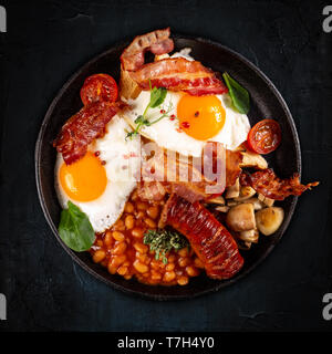 Flat lay of Full English Breakfast including sausages, grilled tomatoes and mushrooms, egg, bacon and baked beans Stock Photo