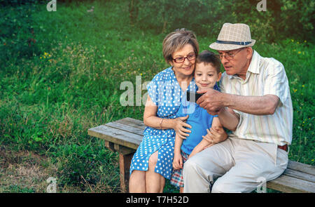 Grandfather taking selfie with grandmother and grandson sitting on a bench Stock Photo