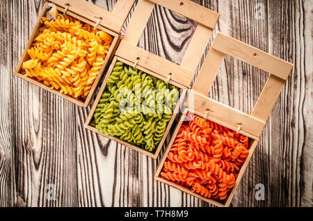 Multi-coloured pasta in the form of spirals lies in square wooden boxes that stand on a wooden table Stock Photo