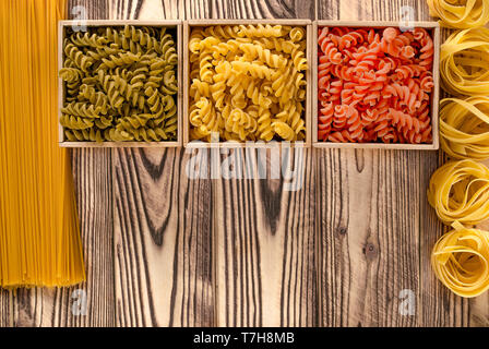 Multi-coloured pasta in the form of spirals lies in square wooden boxes that stand on a wooden table Stock Photo