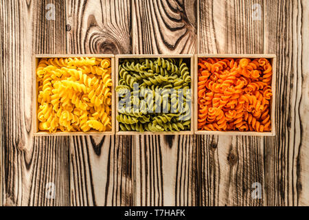 Multi-coloured pasta in the form of spirals lies in square wooden boxes that stand on a wooden table Stock Photo