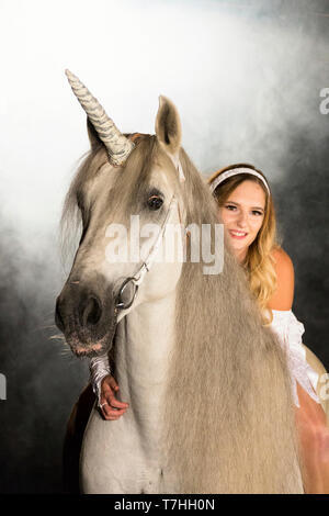 Young woman (fairy, virgin) on back of unicorn (Pure Spanish Horse with attached horn). Germany Stock Photo