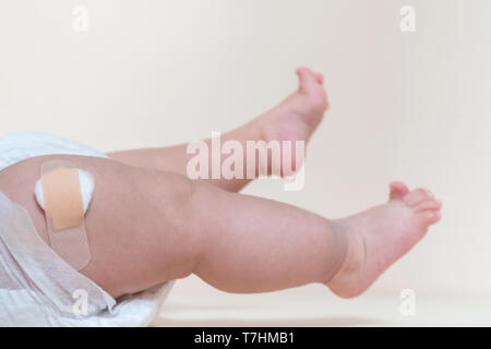 baby boy legs with a band-aid patch after taking a vaccine. doctor or nurse putting plaster on baby leg at the hospital. Stock Photo