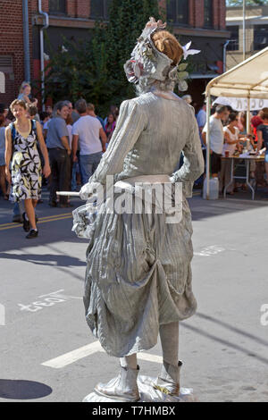 ASHEVILLE, NORTH CAROLINA, USA – 9/5/2010: A popular human statue known as the Silver Drummer Girl busks in downtown Asheville, holding still then com Stock Photo
