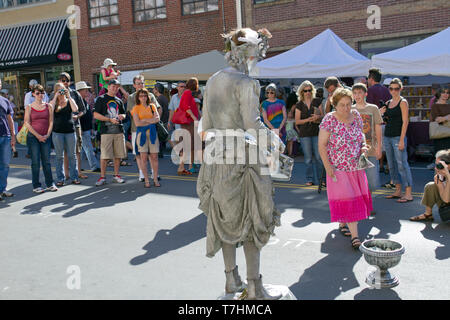 ASHEVILLE, NORTH CAROLINA, USA – 9/5/2010: A popular human statue busker known as the Silver Drummer Girl entertains crowds in the street as she holds Stock Photo