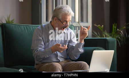 Excited grey haired man surprised by unbelievable news on laptop Stock Photo