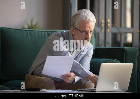 Grey haired mature man calculating bills, using laptop at home Stock Photo