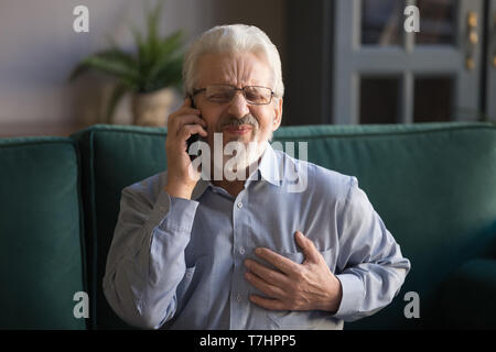 Grey haired man touching chest, having heart attack, calling emergency Stock Photo