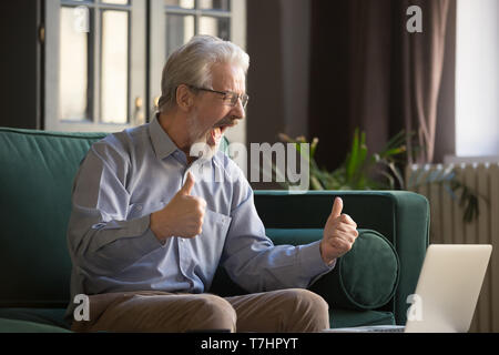 Happy excited grey haired mature man celebrating success, using laptop Stock Photo