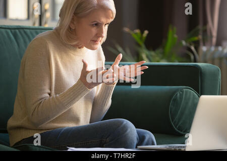 Unhappy grey haired mature woman having problem with laptop at home Stock Photo