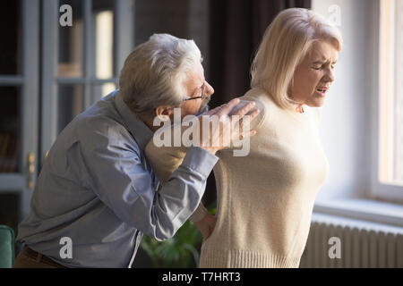 Mature woman suffering from sudden backache, old man supporting her Stock Photo