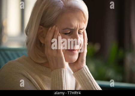 Close up grey haired woman suffering from headache, touching temples Stock Photo