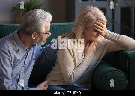 Grey haired husband supporting unhappy mature woman wife at home Stock Photo