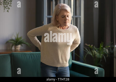 Unhappy grey haired mature woman touching back, suffering from backache Stock Photo