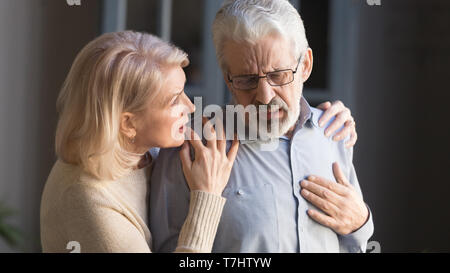 Grey haired man touching chest, having heart attack, woman supporting Stock Photo
