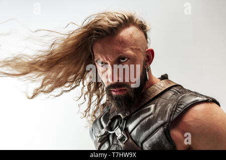 Threatening. Blonde long hair and muscular male model in leather viking's costume with the big hammer cosplaying Thor isolated on white studio background. Fantasy warrior, antique battle concept. Stock Photo