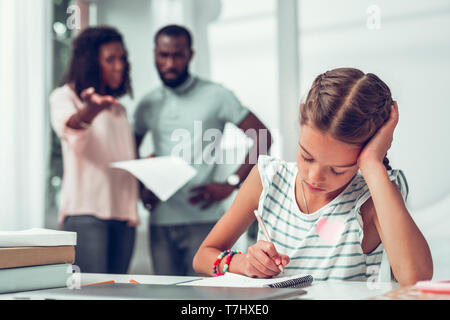 Sad daughter doing home tasks while parents screaming at her. Stock Photo