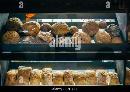 Glass bakery showcase with shelves on which lies bread and buns of various types.