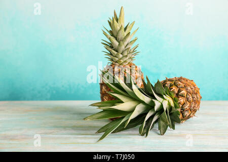 Delicious pineapples on wooden table against color background Stock Photo