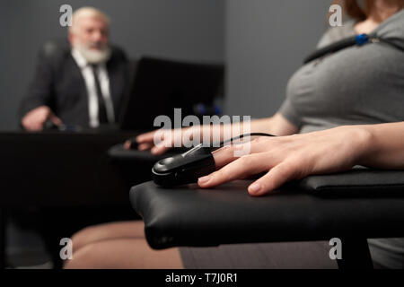 Finger sensor of lie detector on female hand. Sensors and wire for defining of pulse amplitude. Technology for monitoring and testing lie or truth. Concept of defining of honesty. Stock Photo