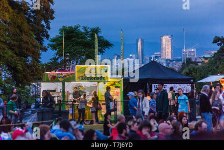 Attendees purchase food and beverages from music festival vendors with the city skyline of Vancouver, British Columbia lit by the sunset beyond. Stock Photo