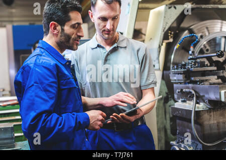Two workers discussing a project in front of CNC lathe machine Stock Photo