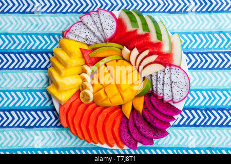 Tropical fruits assortment on a white plate, blue colorful textile background. Top view. Copy space. Stock Photo