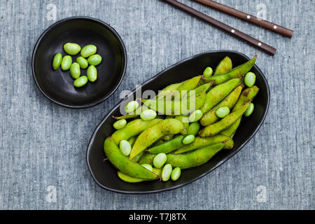 Fresh edamame green beans in black bowl. Grey background. Top view. Copy space. Stock Photo