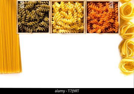 Multi-colored pasta in the form of spirals lie in wooden boxes that stand on a white table. isolated Stock Photo