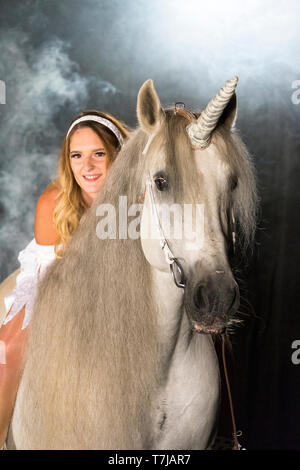 Young woman (fairy, virgin) on back of unicorn (Pure Spanish Horse with attached horn). Germany Stock Photo