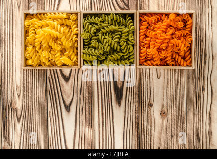 Multi-coloured pasta in the form of spirals lies in square wooden boxes that stand on a wooden table Stock Photo