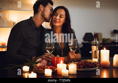 Beautiful passionate couple having a romantic candlelight dinner at home, kissing Stock Photo
