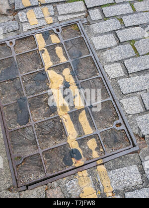 Double yellow lines on cobbled street surface with manhole cover. Stock Photo