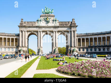 People enjoy a sunny day at the foot of the arcade du Cinquantenaire, the monumental triple arch in the Cinquantenaire park in Brussels, Belgium. Stock Photo