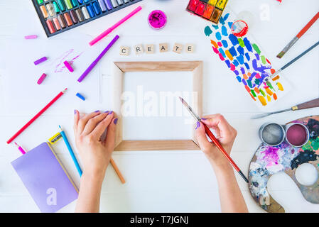 Top view Female Hands holding brush over blank canvas and Create word lettering with many colorful paintiing materials on white background. Add colors Stock Photo