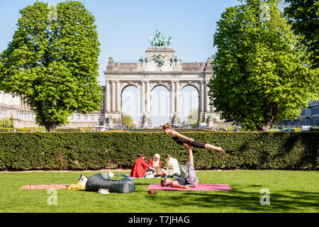 A young couple is practicing acroyoga on the grass in the Cinquantenaire park in Brussels, Belgium, with the arcade du Cinquantenaire in the distance. Stock Photo
