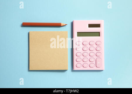 Pink digital calculator and memo note pad and brown colored pencil on blue background Stock Photo
