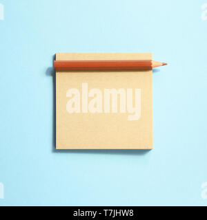 Memo note pad and brown colored pencil on blue background Stock Photo