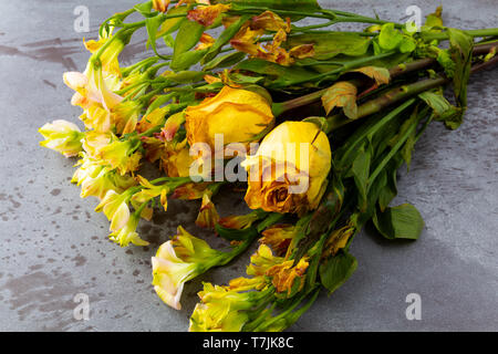 Top view of a bouquet of wilting flowers with yellow roses on a gray background illuminated with natural lighting. Stock Photo