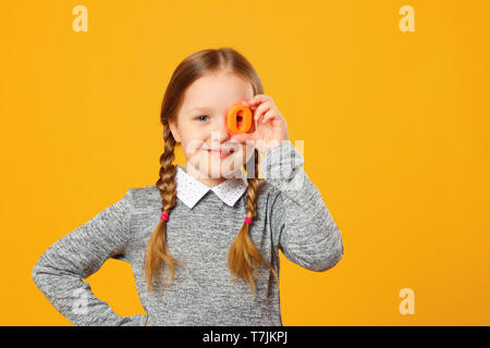 Portrait of a cheerful little child girl on a yellow background. Schoolgirl holds the letter O. The concept of education. Stock Photo