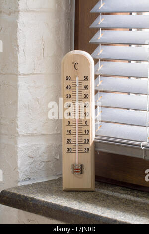 A wooden thermometer with an analog scale measuring the temperature placed near the window Stock Photo