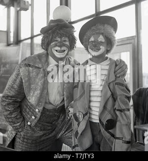 1960s, historical, all smiles...having fun at school, a circus clown vistin a primary school poses for a photo beside a smiling young schoolboy in fancy dress and with his face painted as a clown, England, UK. Stock Photo