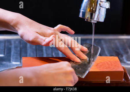 woman professional chef hands hold knife for whetting on whetstone.premium professional stone from japan.knife sharpening process with traditional sha Stock Photo