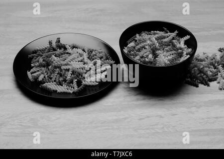 delicious colorful Italian pasta in two black ceramic plates on grey textured background, side view Stock Photo