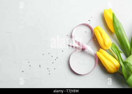 8 March, International Women's Day. Figure eight of pink ribbon with beautiful yellow tulips on gray background. Space for text Stock Photo