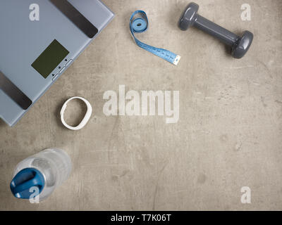 Closeup on laying on the floor weight scales, grey dumbbell, white fitness tracker, bottle of water, tape measure. Stock Photo