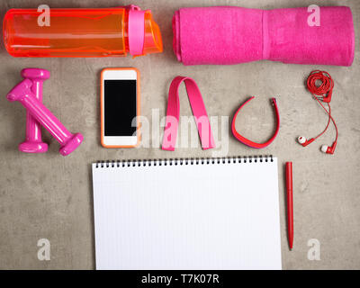Closeup on pink dumbbells, towel, bottle of water, headphones, fitness tracker, elastic band, smartphone and opened notebook with pen laying on the fl Stock Photo
